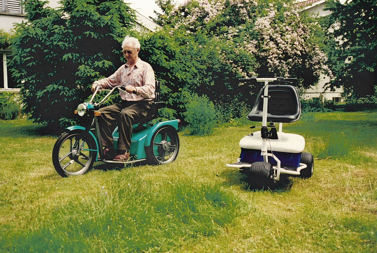 Sur la gauche, on peut voir un véhicule vert avec une personne âgée sur la pelouse. À droite, une Golfmobile blanche.