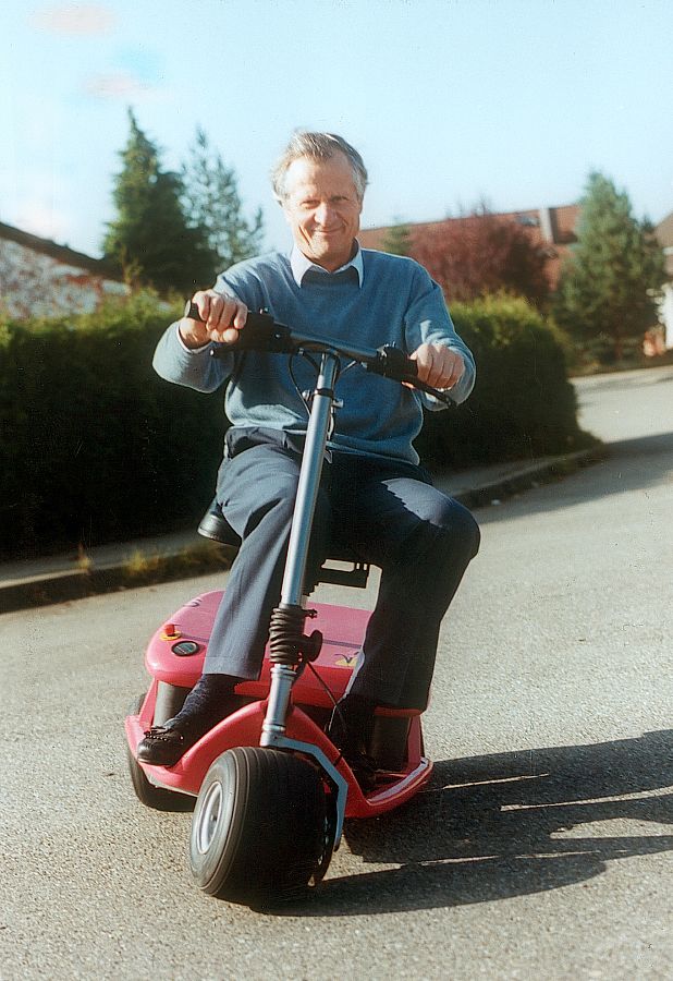 A man on one of Martin Kyburz's first electric golfmobiles, a road and a bush in the background.